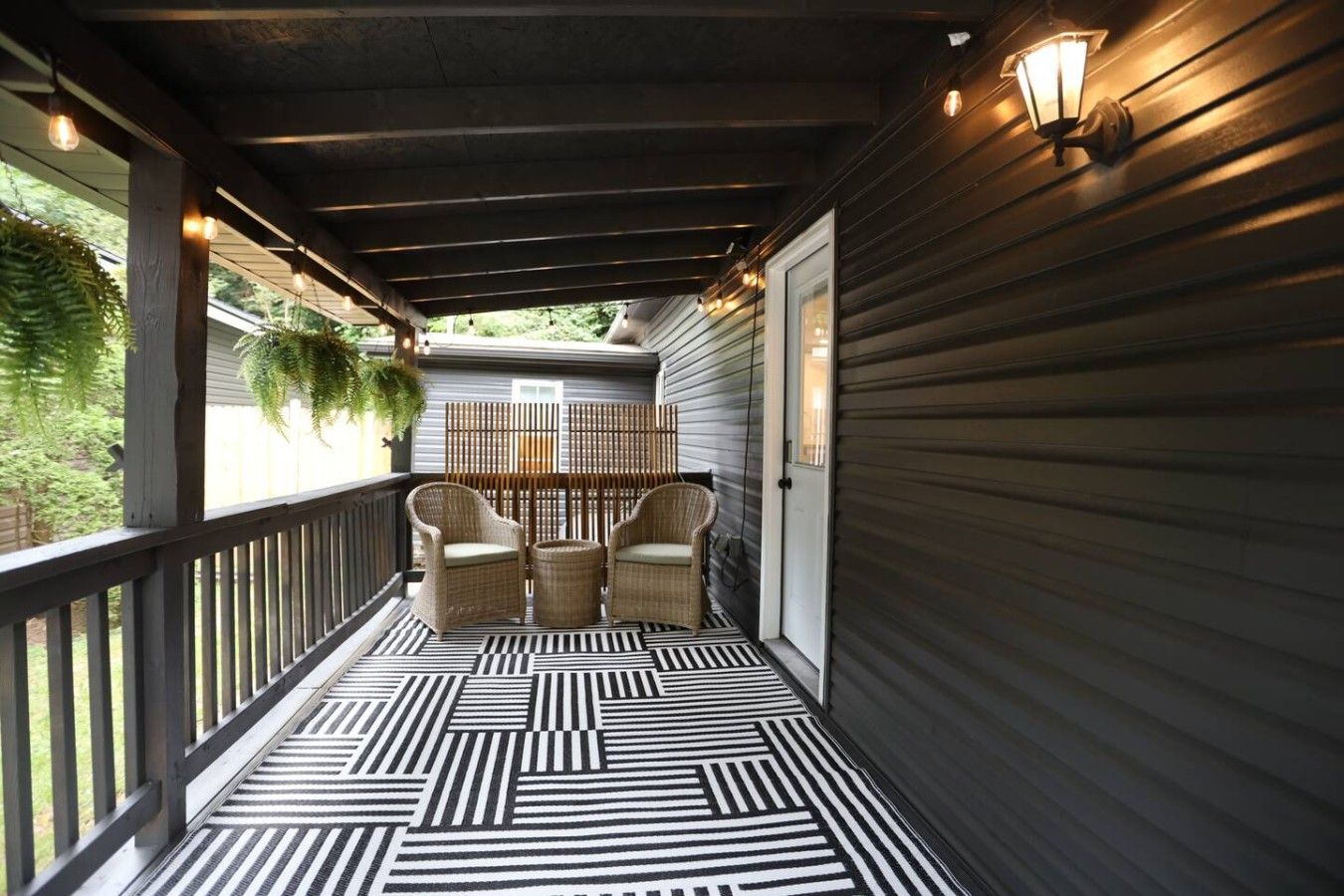 A covered porch with a patterned floor, two wicker chairs, and a wall-mounted light fixture.