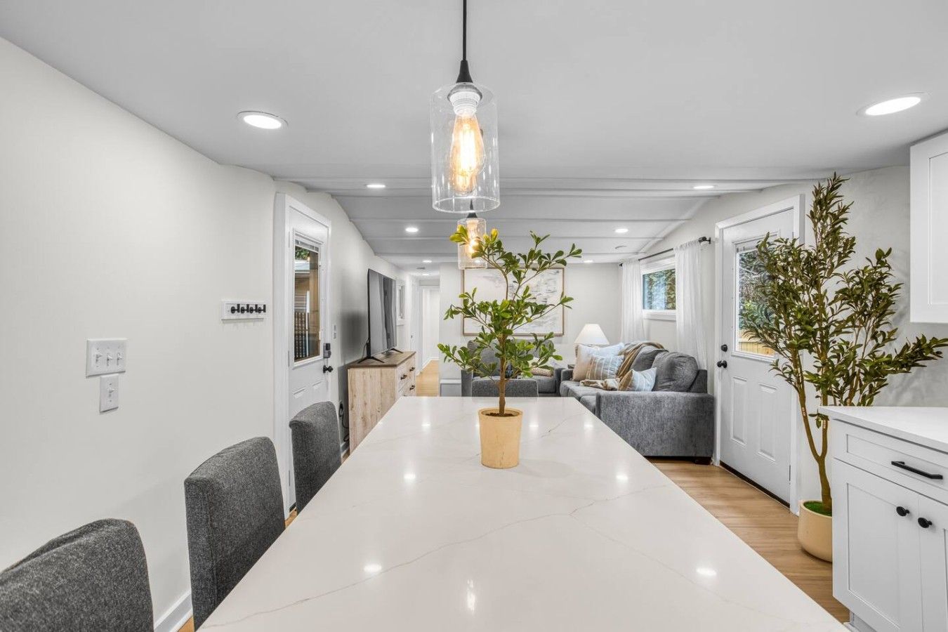 A modern kitchen with white cabinets, a marble countertop, and a hanging pendant light.