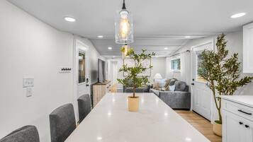 A modern kitchen with white cabinets, a marble countertop, and a hanging pendant light.