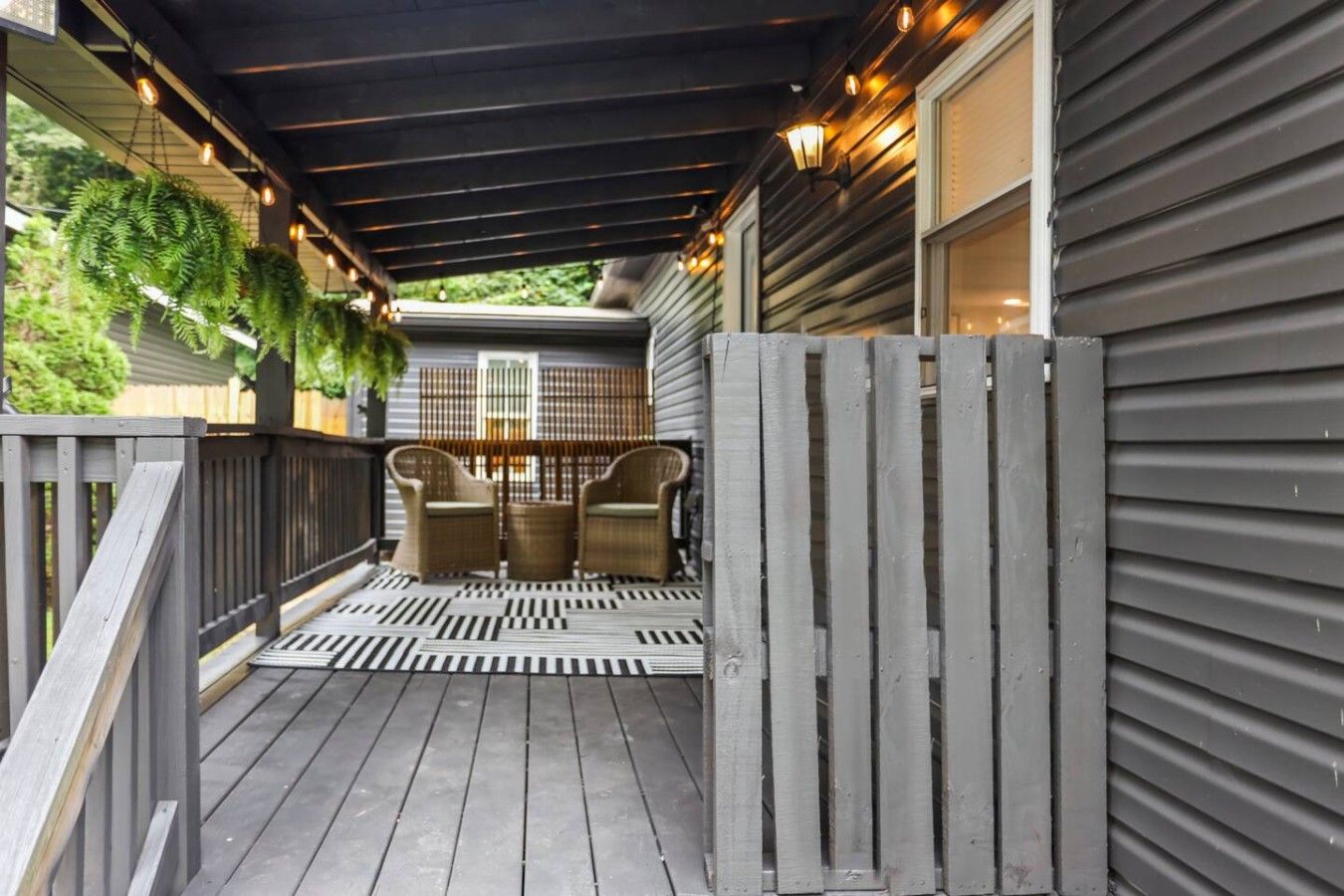 Eine überdachte Veranda mit Holzterrasse, zwei Korbstühlen und einem dekorativen Zaun.