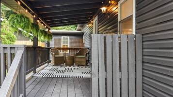 Eine überdachte Veranda mit Holzterrasse, zwei Korbstühlen und einem dekorativen Zaun.