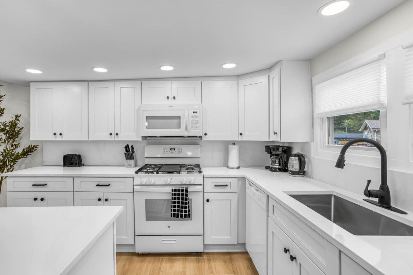 A modern kitchen with white cabinets, a gas stove, a microwave, and a sink.