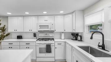A modern kitchen with white cabinets, a gas stove, a microwave, and a sink.