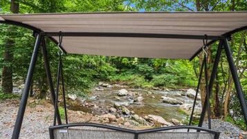 A covered outdoor seating area with a view of a stream and forest.