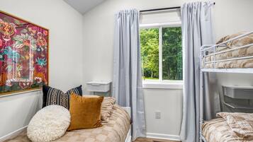 Un dormitorio con una cama litera, una mesita de noche, una ventana con cortinas y un cuadro de colores en la pared.