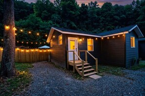 A small cabin with a wooden staircase leading to a door, surrounded by a gravel path and a wooden fence.