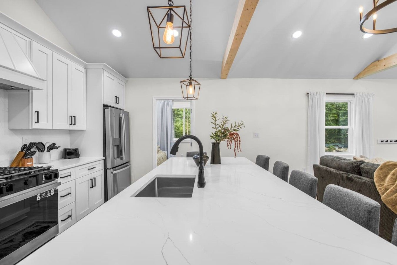 A modern kitchen with white cabinetry, a central island, and a dining area with grey upholstered chairs.