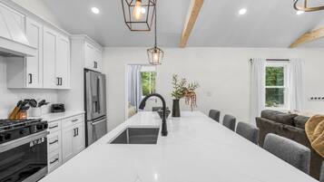 A modern kitchen with white cabinetry, a central island, and a dining area with grey upholstered chairs.