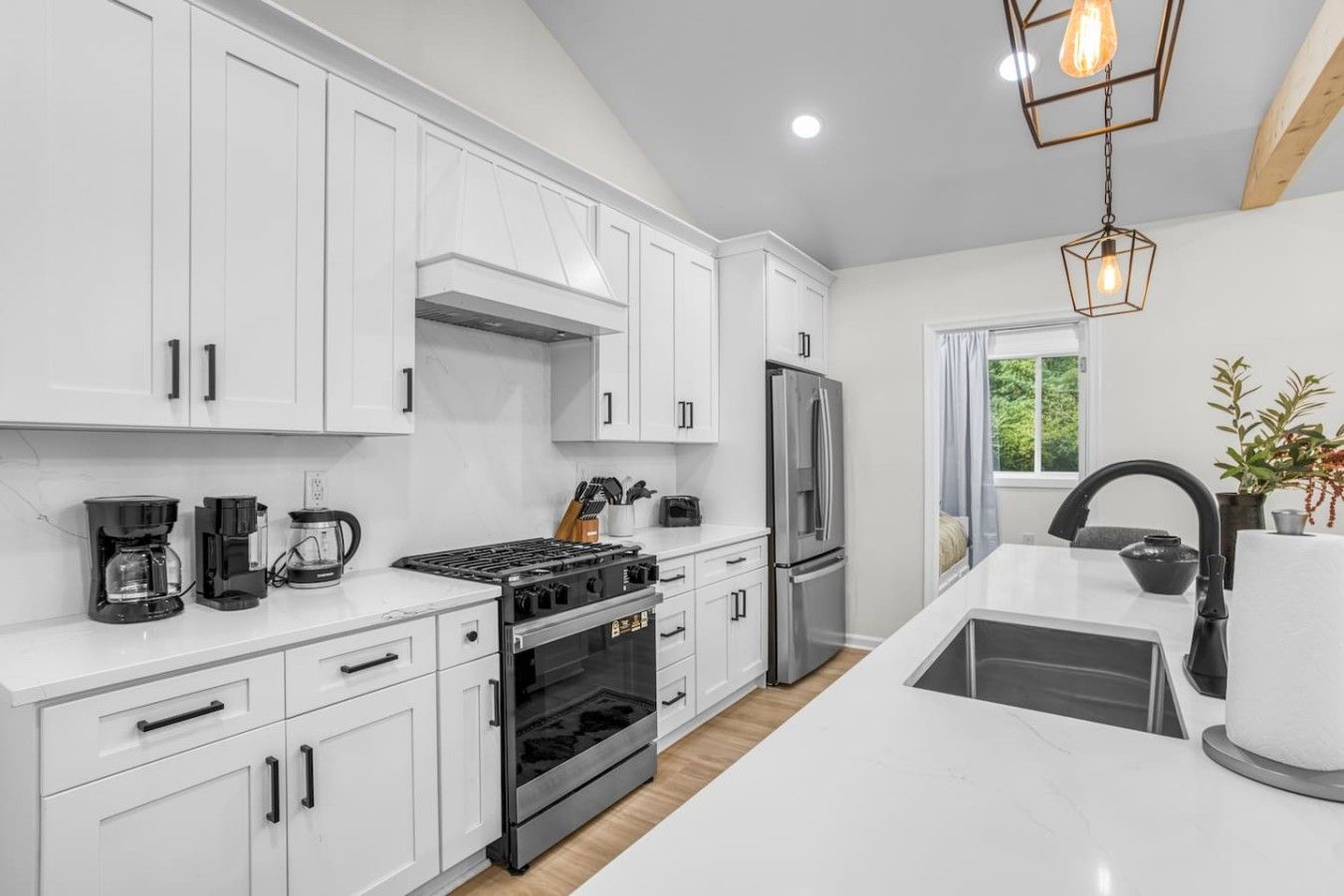 Une cuisine moderne avec des meubles blancs, un réfrigérateur en acier inoxydable, une cuisinière à gaz et un four encastré.
