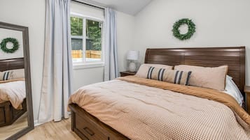 A bedroom with a wooden bed, a window with curtains, a nightstand with a lamp, and a wall-mounted wreath.