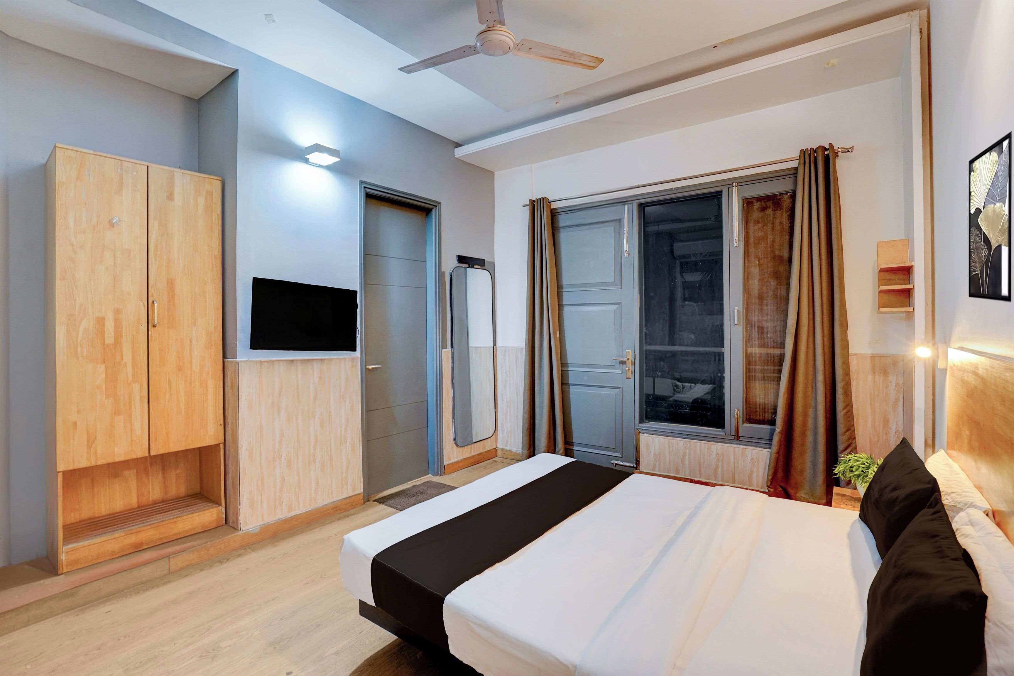 A modern hotel room with a bed, wardrobe, television, and a sliding door to a balcony.