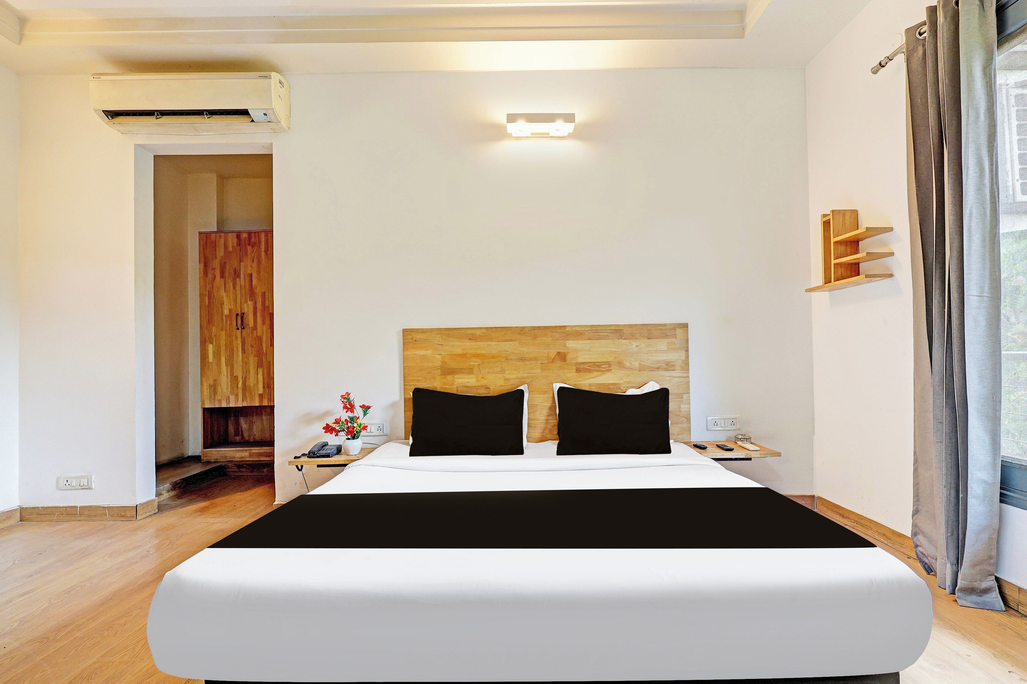 A hotel room with a large bed, a wooden headboard, a bedside table with a phone and remote, and a nightstand with a lamp.
