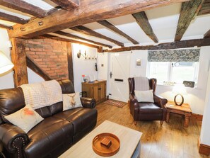 A cozy living room with a leather sofa, a wooden coffee table, and a leather armchair. - Lilac Cottage (Rugby)
