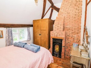 A bedroom with a brick fireplace, wooden wardrobe, and a bed with rolled towels. - Lilac Cottage (Rugby)