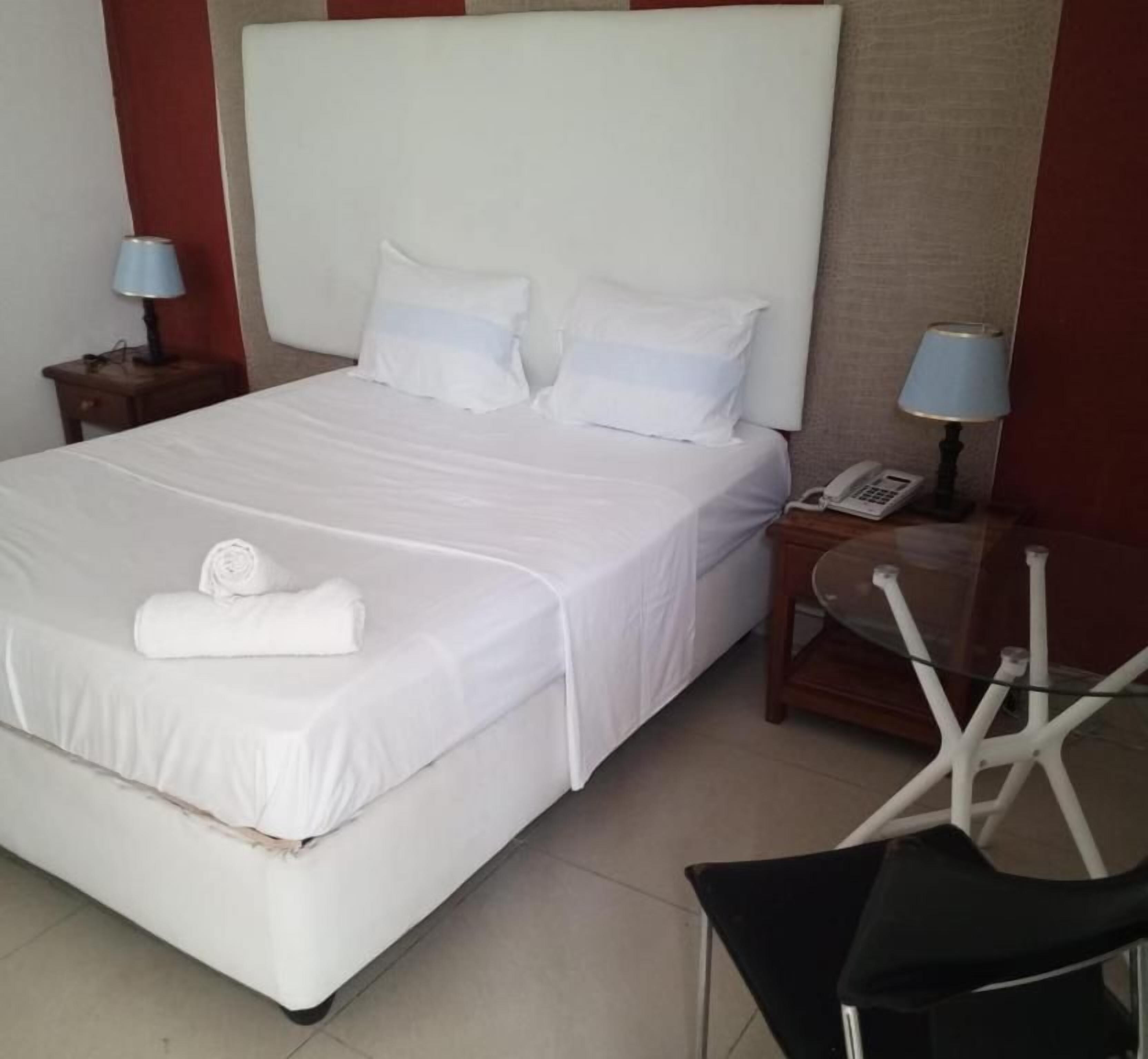A hotel room with a large bed, two bedside tables, a chair, and a telephone.