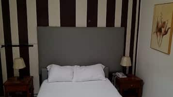 Un cuarto de hotel con una cama grande, dos mesitas de noche, una lámpara sobre cada una y un teléfono en una de ellas, además de un cuadro en la pared.