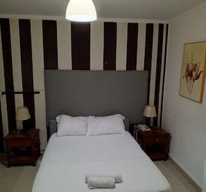 A hotel room with a large bed, two bedside tables, a lamp on each table, a telephone on one table, and a painting on the wall. - Angola Stay Connect (Luanda)