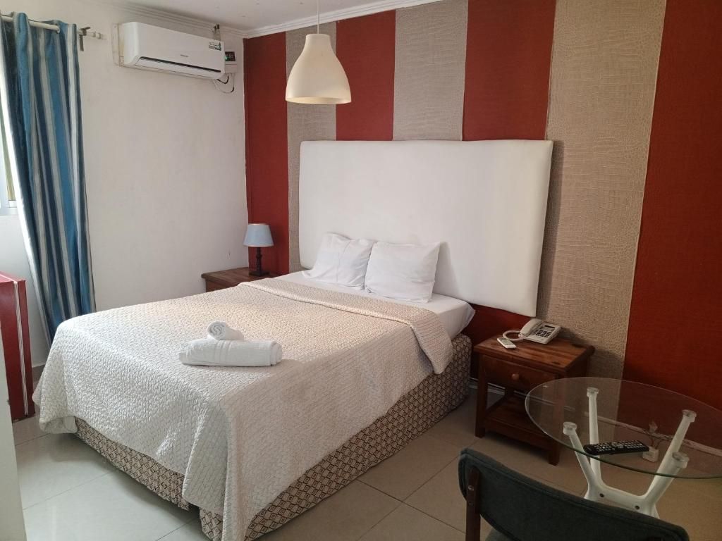 Habitación de hotel con cama, mesita de noche, lámpara y una mesa de vidrio con control remoto.