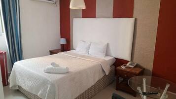 Habitación de hotel con cama, mesita de noche, lámpara y una mesa de vidrio con control remoto.