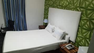 Una habitación de hotel con cama, mesita de noche con lámpara, teléfono y pared texturizada verde.