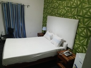 Una habitación de hotel con cama, mesita de noche con lámpara, teléfono y pared texturizada verde.
