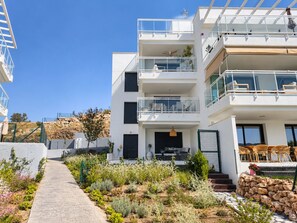 A multi-story residential building with balconies, a paved pathway, and a landscaped garden. - La Casa Eliana 3-bedroom Apartment (AN)