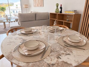 A dining table set with plates, cutlery, and glassware, with a bookshelf and a sofa in the background. - La Casa Eliana 3-bedroom Apartment (AN)