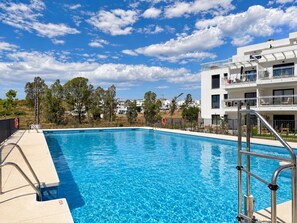 A swimming pool with clear blue water, surrounded by a metal safety ladder, and a modern building with balconies in the background. - La Casa Eliana 3-bedroom Apartment (AN)