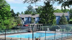 Una piscina con bordo recintato, poltrone relax e un edificio sullo sfondo.