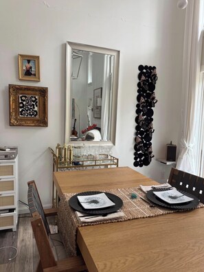 A dining area with a wooden table, chairs, a mirror, and wall decorations including a framed picture and a black circular pattern. - Luxurious, light-filled 2 bedroom condo in Bloomington IU Football Fans (Bloomington)