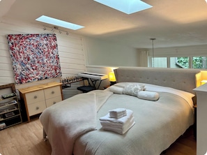 A bedroom with a bed, a desk with a keyboard, a painting, and a skylight. - Luxurious, light-filled 2 bedroom condo in Bloomington IU Football Fans (Bloomington)