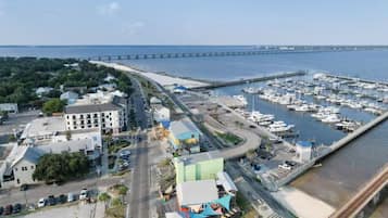An aerial view of a marina with boats docked, a bridge in the background, and a road leading to a building with a green roof.