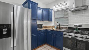 Une cuisine avec des meubles de couleur bleue, un réfrigérateur en acier inoxydable, un four à micro-ondes, un évier et une cuisinière.