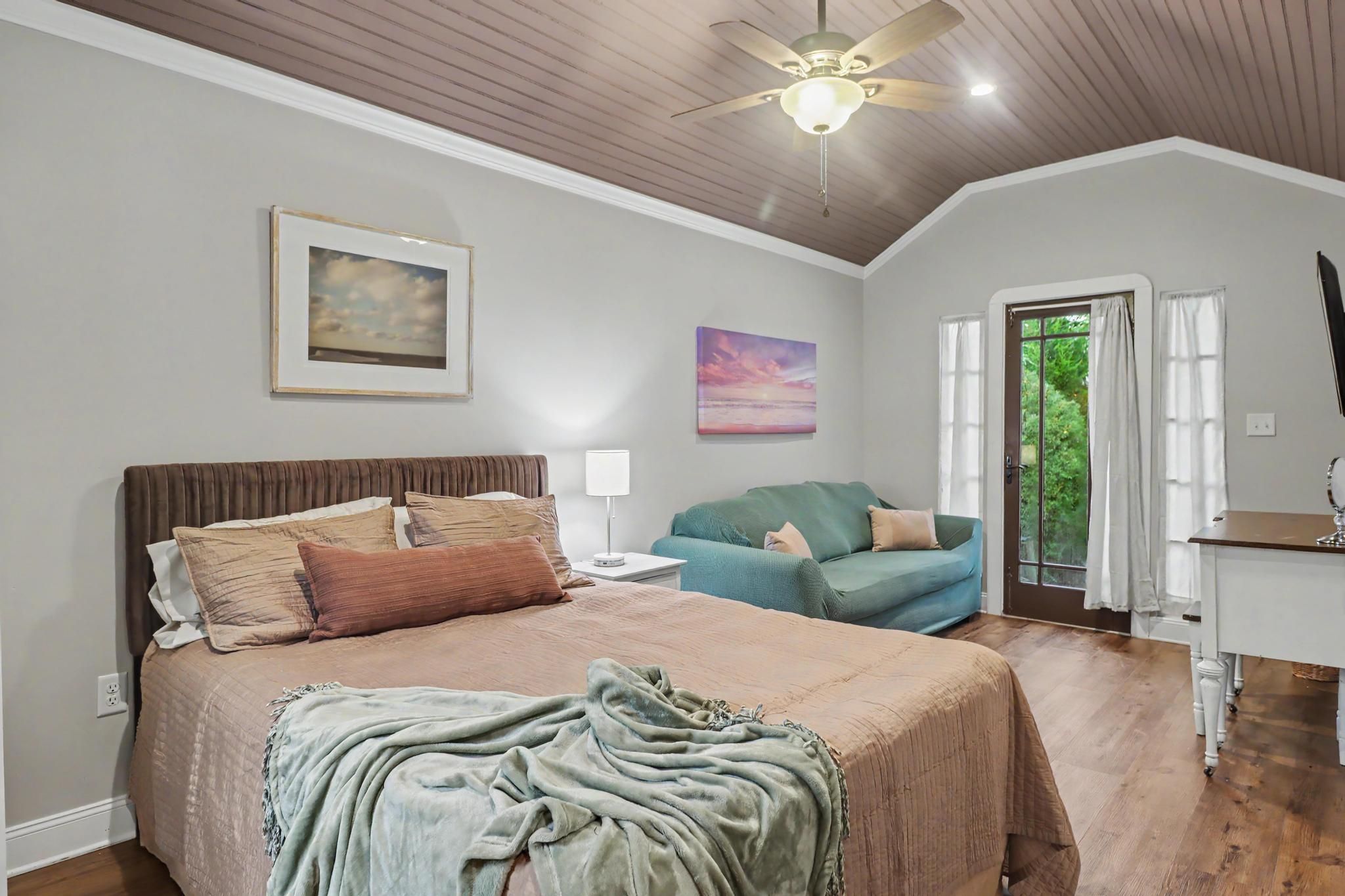 A bedroom with a bed, a nightstand, a lamp, a ceiling fan, and a view of the outdoors through a door.