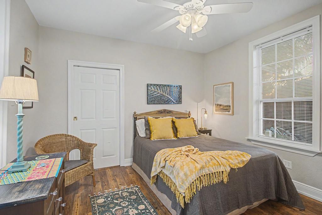 A bedroom with a bed, a chair, a desk, a lamp, a ceiling fan, and a window with blinds.