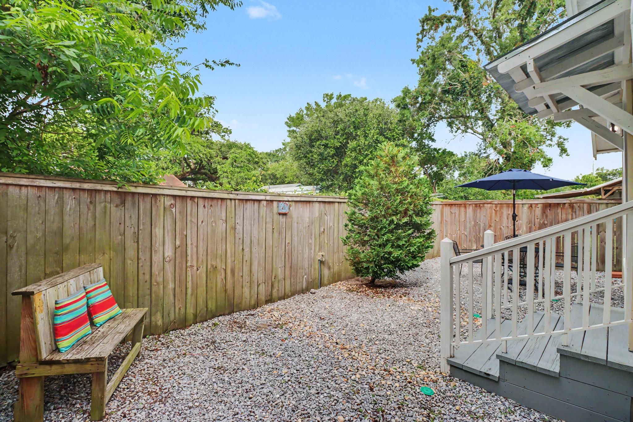 A wooden deck with a bench and a small tree, surrounded by a wooden fence and gravel.