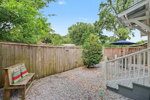 A wooden deck with a bench and a small tree, surrounded by a wooden fence and gravel.