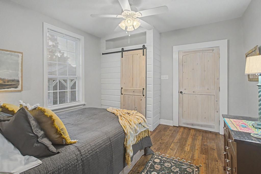 Un dormitorio con cama, ventilador de techo, ventana con persianas, una puerta y cómoda.