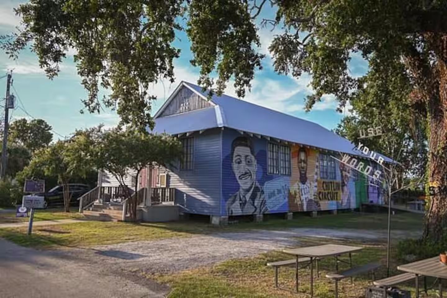 Un edificio con un mural en la fachada, un porche cubierto y un camino de grava que conduce a la entrada.