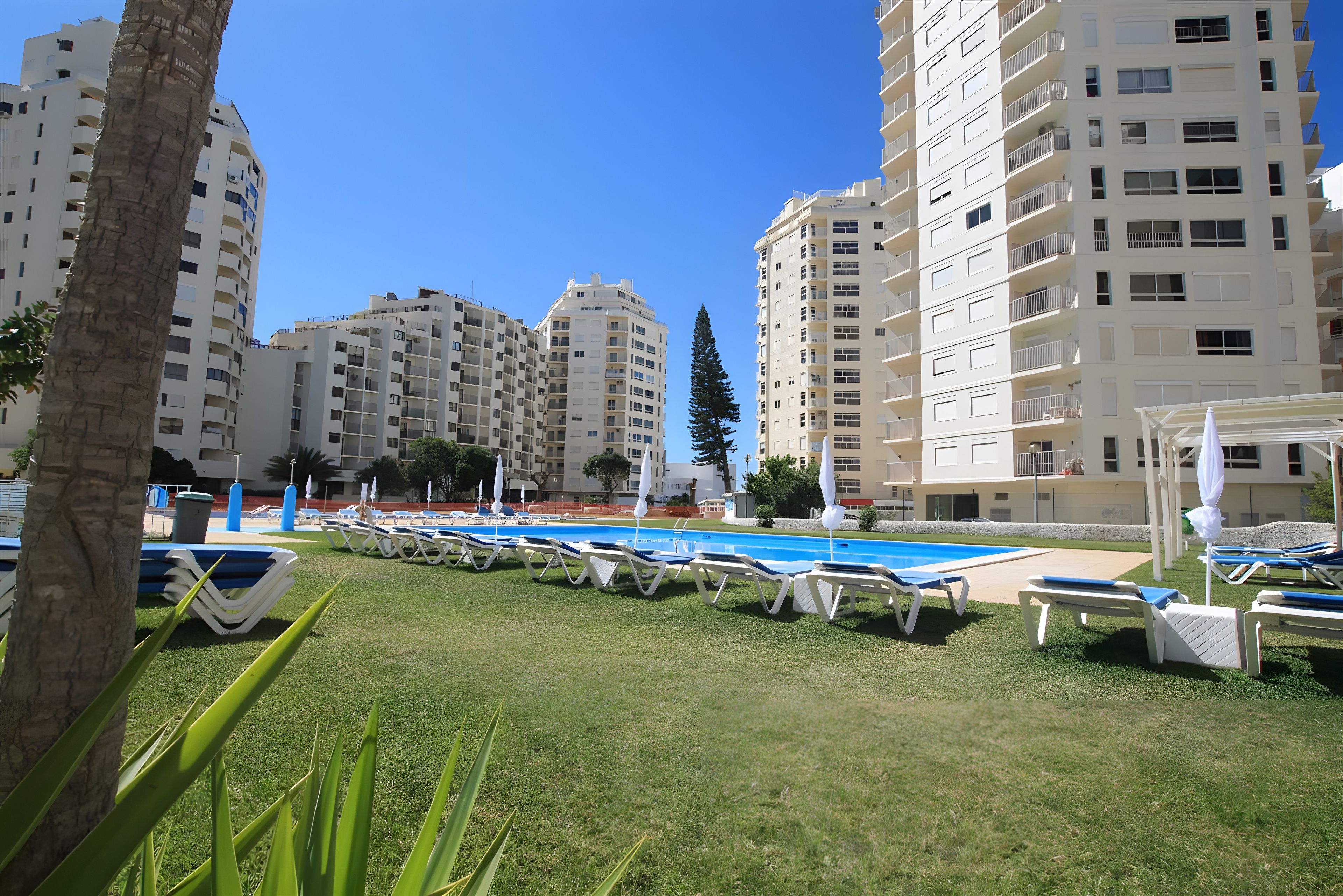A pool area with lounge chairs and a clear blue sky.
