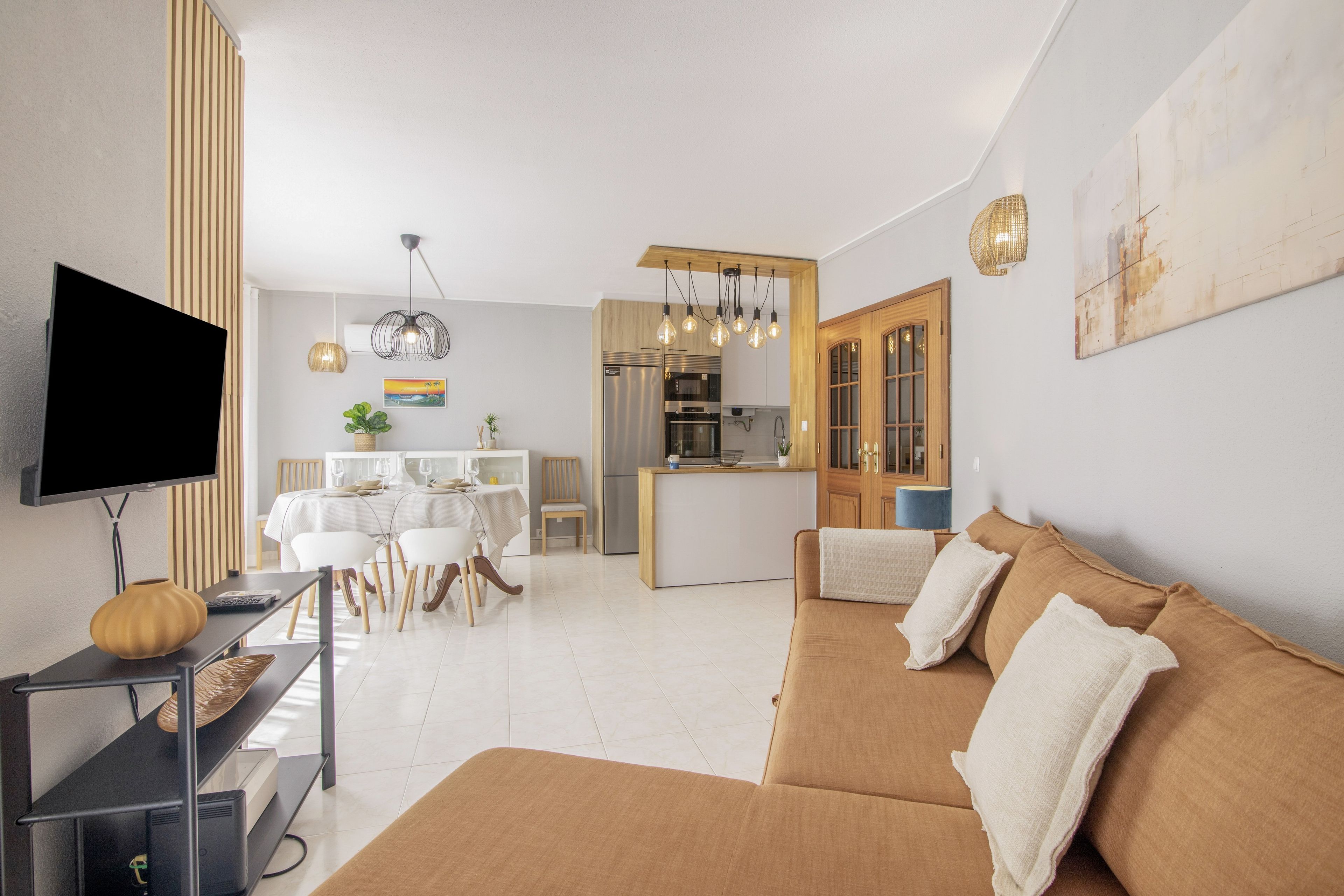 A modern living room with a sofa, a flat-screen TV, and a dining area with a table and chairs.