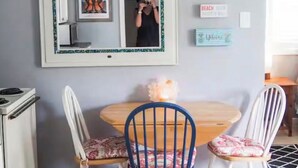 Ein Zimmer mit Esstisch, zwei Stühlen, einem Spiegel und einer kleinen Kommode.
