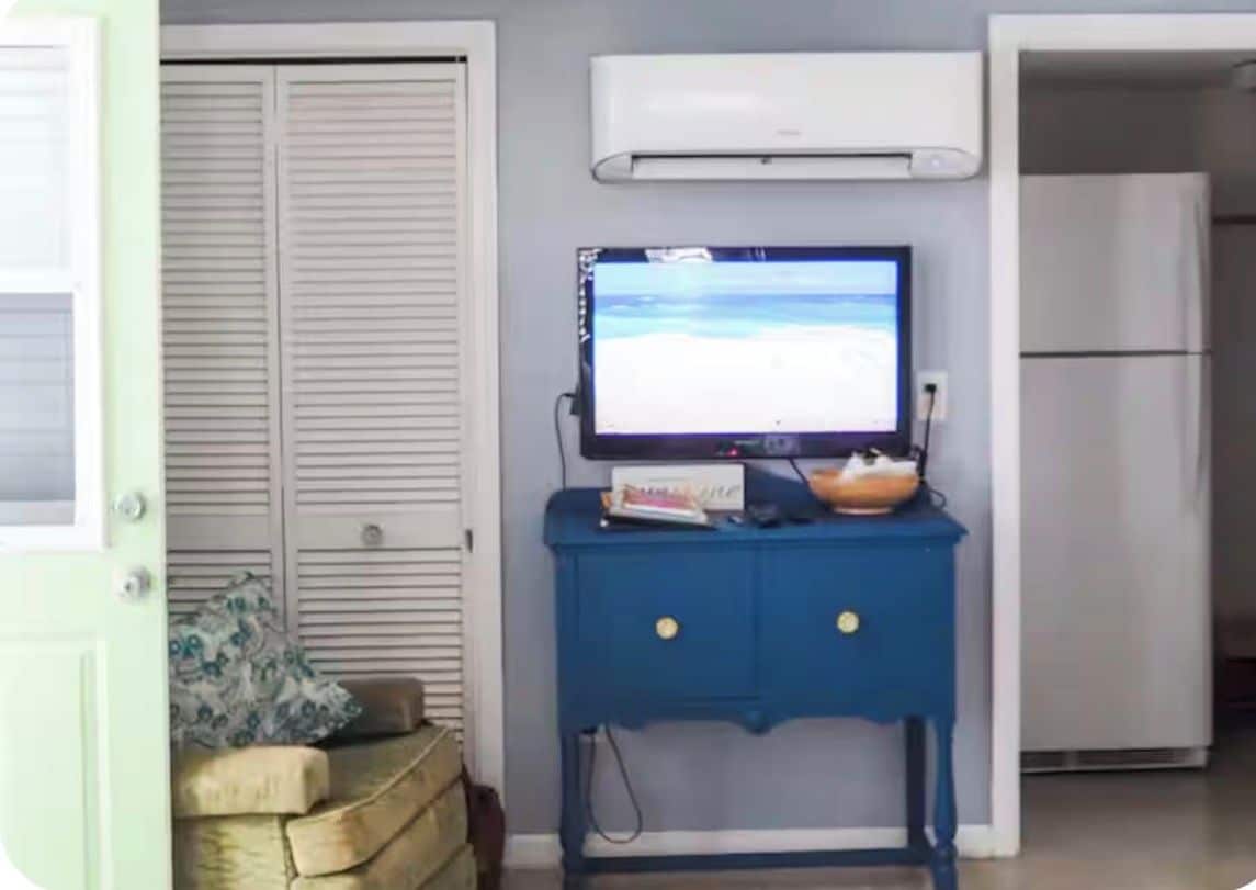 Een kamer met een gesloten deur, een blauwe kast met een televisie en een witte koelkast.