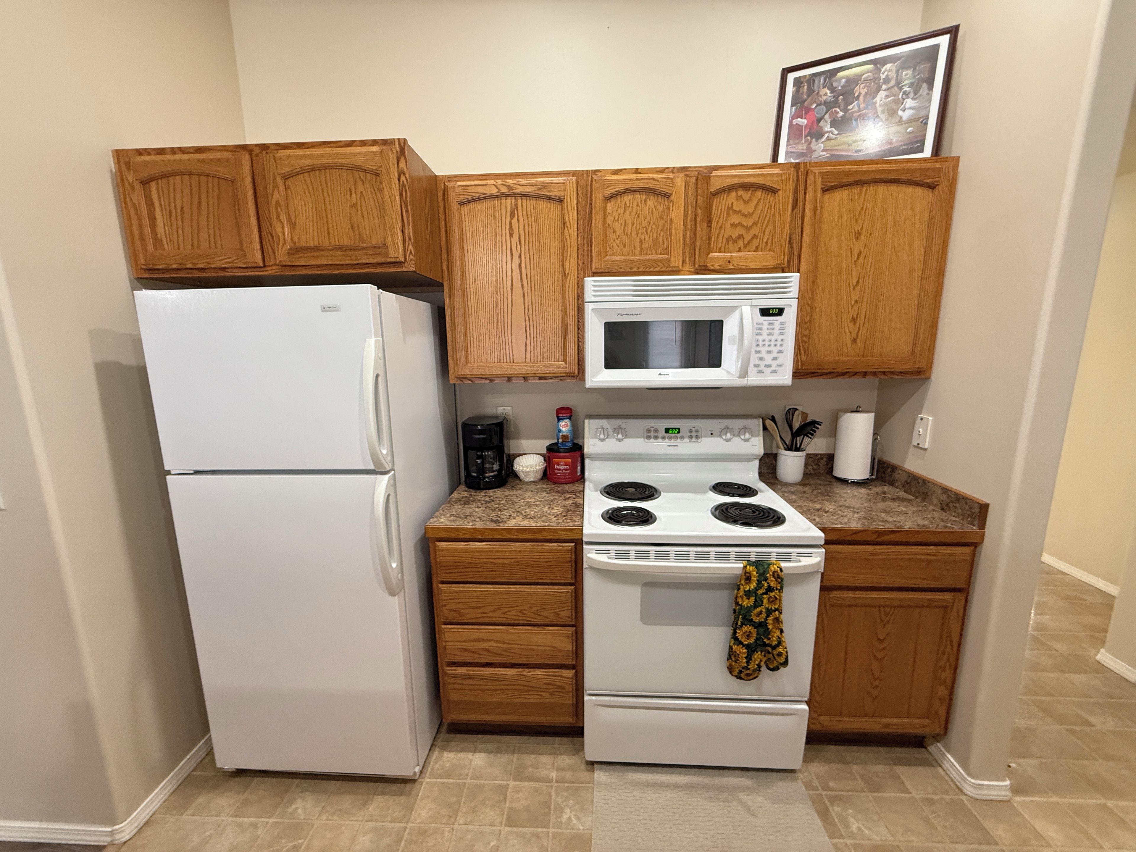 A compact kitchen with wooden cabinets, a white refrigerator, a microwave, and a stove.