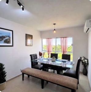 A dining area with a glass table, black chairs, a bench, and a view through large windows with pink curtains. - Exclusive Penthouse | 20 minutes from Boca and Veracruz (Veracruz)