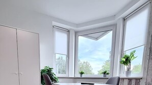 Ein Essbereich mit einem weißen Tisch und zwei Stühlen, einem weißen Kleiderschrank und einem Fenster mit Blick auf Bäume.