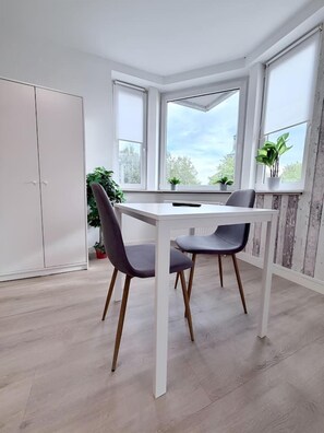 A dining area with a white table and two chairs, a white wardrobe, and a window with a view of trees. - City View II Vacation Rental – Terrace & Downtown (Nordhorn)