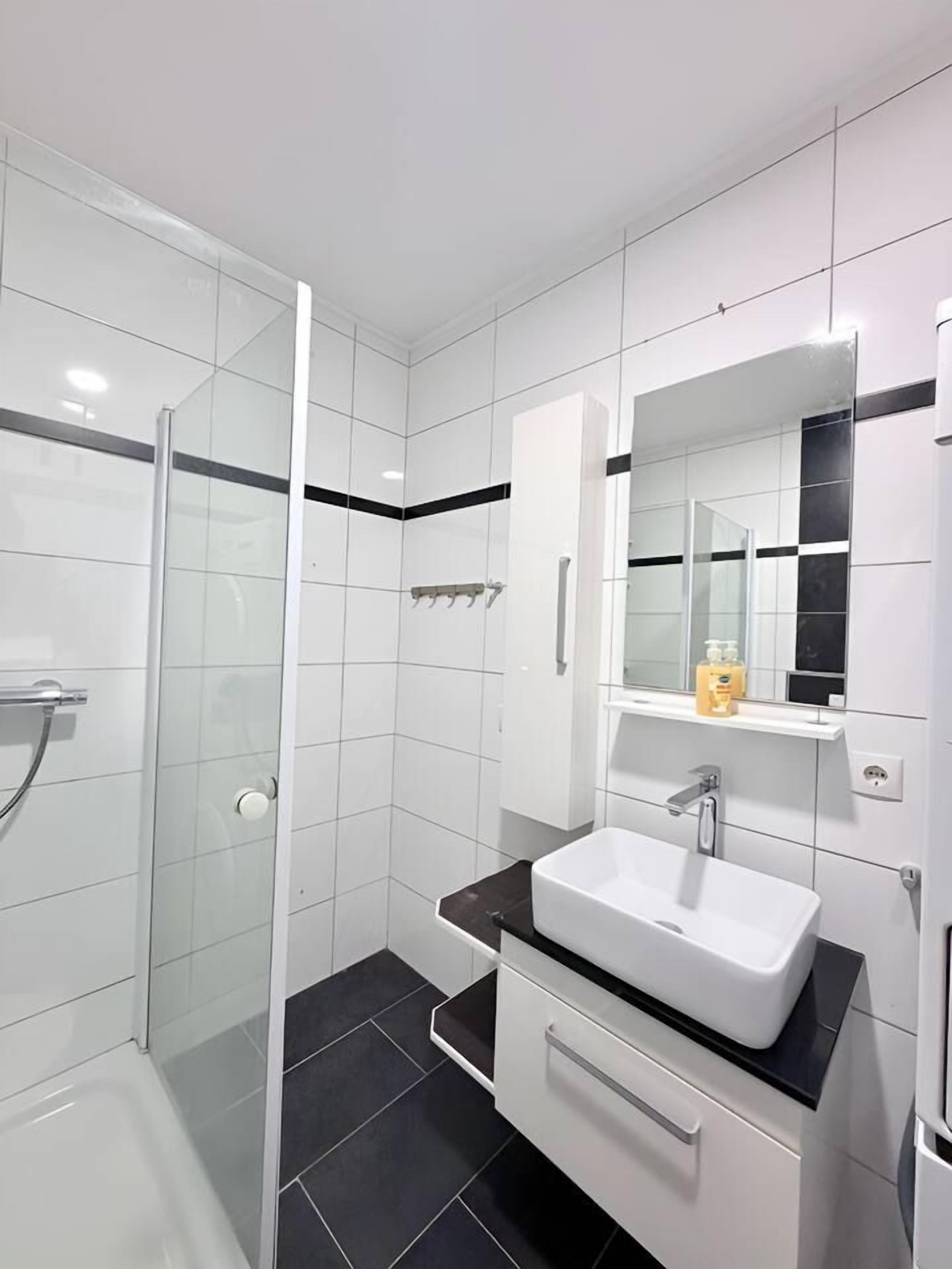 Ein modernes Badezimmer mit einer gläsernen Dusche, einem weißen Waschbecken und einem Spiegel darüber.