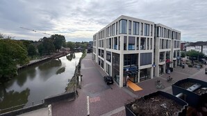 Ein modernes Gebäude mit Glasfassade, vor dem sich ein Kanal erstreckt, und ein Fußweg.