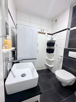 A modern bathroom with a white sink, a toilet, and a built-in cabinet. - City View II Vacation Rental – Terrace & Downtown (Nordhorn)